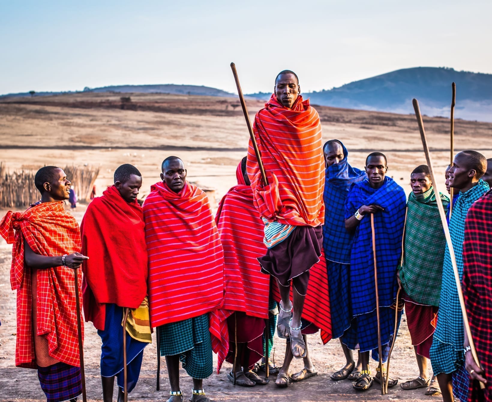 A group of Maasai men and women in red and blue shukas standing with walking staffs