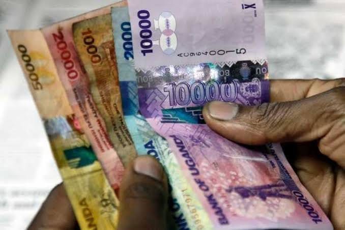 A hand holding a fan of Ugandan shilling banknotes of several denominations